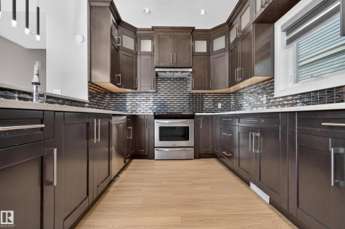 Integrated stainless steel appliances, dark wood-finish cabinetry, light wood-finish flooring, textured tile backsplash, and light-toned countertops - 11167 62 Avenue Nw, Edmonton, AB 