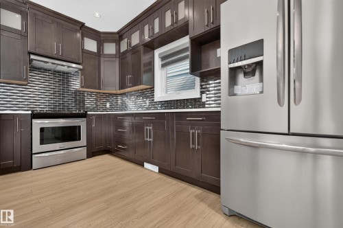Kitchen featuring dark wood-finish cabinetry, stainless steel appliances, a textured tile backsplash, white countertops, and wood-finish flooring - 11167 62 Avenue Nw, Edmonton, AB 
