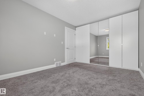 Wall-to-wall carpeting in a neutral tone, white painted baseboards, paneled interior door, and built-in closet with mirrored and solid white doors - 11167 62 Avenue Nw, Edmonton, AB 
