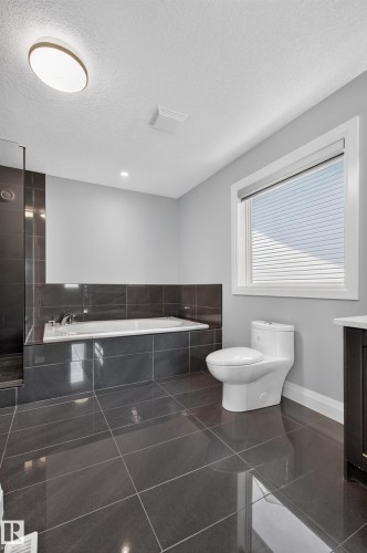 Large format dark tile flooring, built-in bathtub with dark tile surround, separate shower with dark tile, white toilet, and recessed lighting - 11167 62 Avenue Nw, Edmonton, AB 