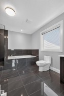 Large format dark tile flooring, built-in bathtub with dark tile surround, separate shower with dark tile, white toilet, and recessed lighting - 