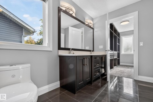Dark wood-finish vanity with dual sinks, a large mirror, and wall-mounted lighting fixtures - 11167 62 Avenue Nw, Edmonton, AB 