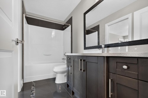 Dark-finish vanity with ample storage and a light-toned countertop, complemented by a decorative framed mirror - 11167 62 Avenue Nw, Edmonton, AB 