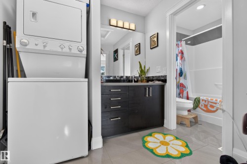 Stackable washer and dryer, dark wood-finish vanity with countertop, large wall mirror, and modern lighting fixture - 11167 62 Avenue Nw, Edmonton, AB 