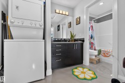 Stackable washer and dryer, dark wood-finish vanity with countertop, large wall mirror, and modern lighting fixture - 