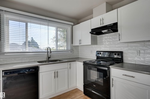 White shaker-style cabinetry with matte black hardware, stone-finish countertops, subway tile backsplash, and wood-finish flooring - 13815 88 Street Nw, Edmonton, AB 