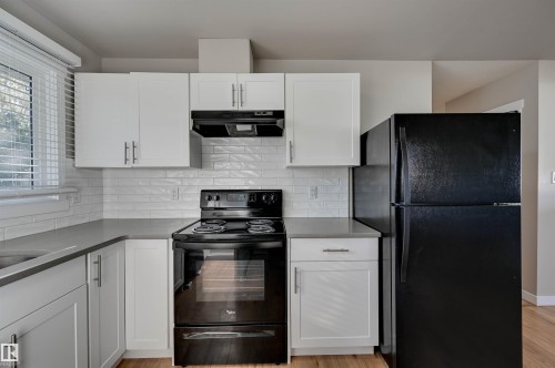 Modern kitchen featuring white upper cabinetry, light gray lower cabinetry, and a white subway tile backsplash - 13815 88 Street Nw, Edmonton, AB 