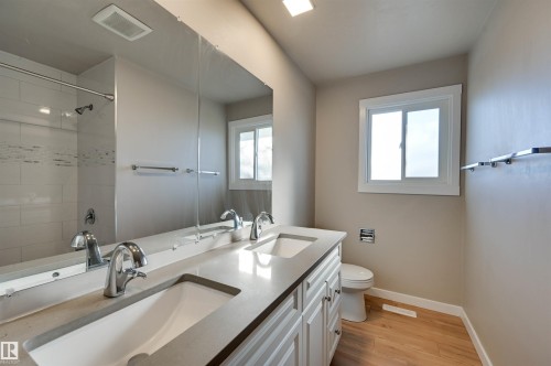 Bathroom featuring a dual vanity with undermount sinks, wood-finish flooring, a window, and a tiled shower - 13815 88 Street Nw, Edmonton, AB 