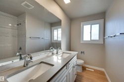 Bathroom featuring a dual vanity with undermount sinks, wood-finish flooring, a window, and a tiled shower - 