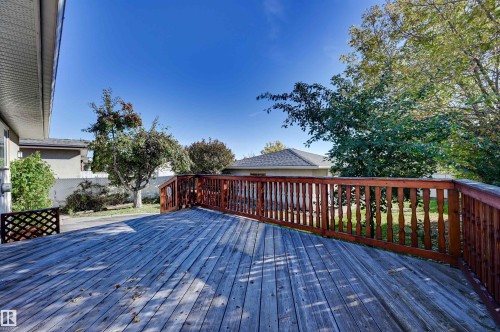 Expansive wood deck with a stained wood railing, featuring a clear sky backdrop and mature landscaping - 13815 88 Street Nw, Edmonton, AB 