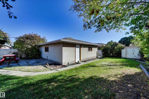 Expansive outdoor space featuring a detached building with stucco siding, a dedicated concrete patio, and a separate storage shed - 13815 88 Street Nw, Edmonton, AB 