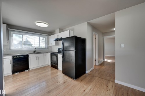 Updated kitchen featuring wood-finish flooring, white cabinetry, a black appliance suite, and a large window above the sink - 13815 88 Street Nw, Edmonton, AB 