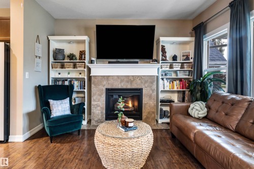 Fireplace with tile surround and mantel, built-in shelving, wood-finish flooring, and large windows - 337 Southfork Drive, Leduc, AB 