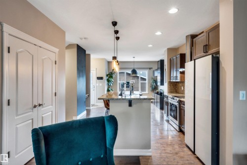 Kitchen featuring a granite-top island, pendant lighting, stainless steel appliances, wood-finish flooring, and cabinetry with dark hardware - 337 Southfork Drive, Leduc, AB 