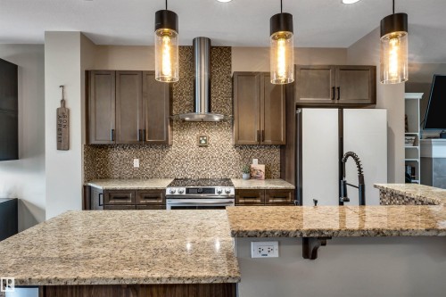 Kitchen featuring wood-finish cabinetry, stainless steel appliances, granite countertops, mosaic tile backsplash, and three pendant light fixtures - 337 Southfork Drive, Leduc, AB 
