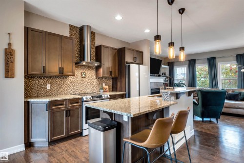 Kitchen featuring wood-finish flooring, dark wood cabinetry, a mosaic tile backsplash, and light-toned countertops - 337 Southfork Drive, Leduc, AB 