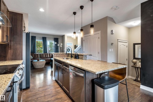 Gourmet kitchen featuring granite countertops, a mosaic tile backsplash, wood-finish flooring, dark wood cabinetry, and stainless steel appliances - 337 Southfork Drive, Leduc, AB 