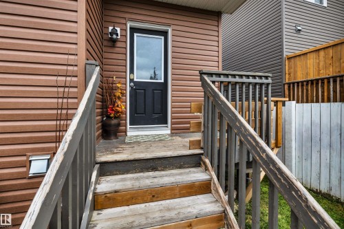 Brown horizontal siding with a black entry door, featuring a window and a wall-mounted light fixture - 337 Southfork Drive, Leduc, AB 