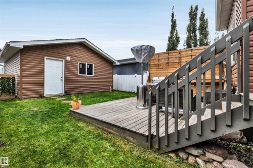 Expansive backyard featuring a manicured lawn, a detached building with horizontal siding, and a wooden deck with railing - 337 Southfork Drive, Leduc, AB 