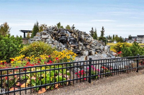 Rock waterfall feature with surrounding landscaping and a black metal fence - 337 Southfork Drive, Leduc, AB 