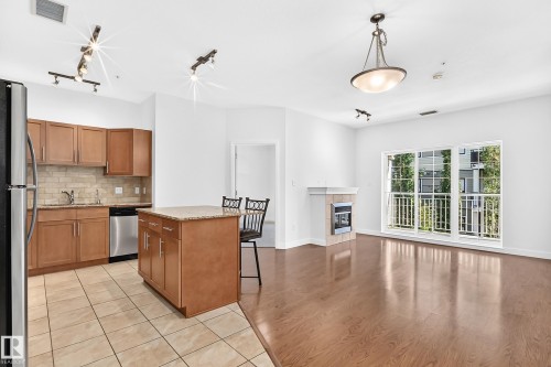 Kitchen island with granite countertop, wood-finish cabinetry, stainless steel appliances, and tile flooring - #307 1003 Gault Bv Nw, Edmonton, AB 