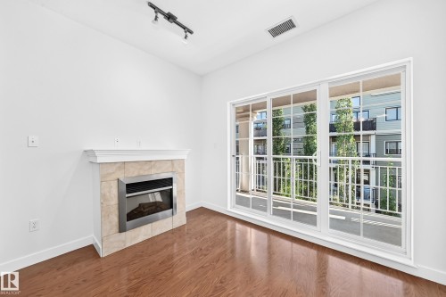 Wood-finish flooring, white walls, built-in fireplace with tile surround, track lighting, and a large sliding glass door with balcony access - #307 1003 Gault Bv Nw, Edmonton, AB 