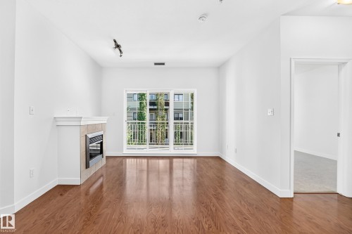 Rich wood-finish flooring, white walls, and a built-in fireplace with a tile surround - #307 1003 Gault Bv Nw, Edmonton, AB 