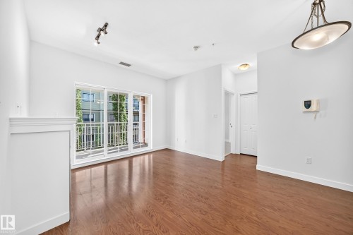 Hardwood-finish flooring throughout, bright white walls, sliding glass doors to a balcony, and a multi-track ceiling light fixture - #307 1003 Gault Bv Nw, Edmonton, AB 