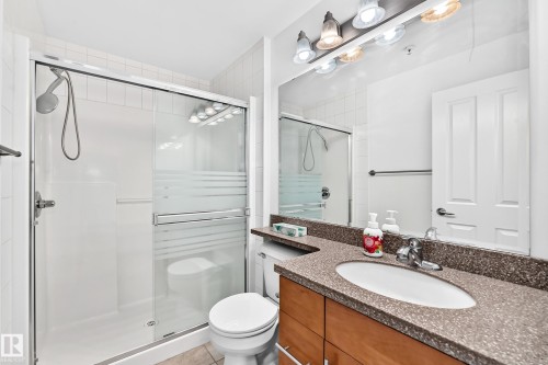 Walk-in shower with sliding glass door, vanity with an integrated sink, polished chrome faucet, and stone-finish countertop - #307 1003 Gault Bv Nw, Edmonton, AB 