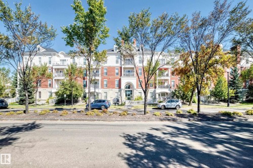 Multi-story building featuring a brick and stone facade, private balconies, a central arched entry, and a pitched roofline - #307 1003 Gault Bv Nw, Edmonton, AB 