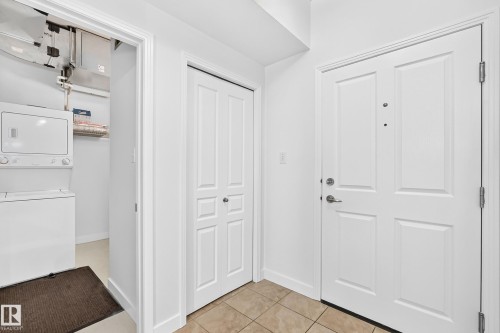 Entryway featuring panel-style doors, tile flooring, and a laundry closet with a stacked washer and dryer - #307 1003 Gault Bv Nw, Edmonton, AB 