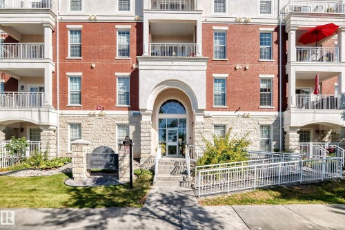 Brick and stone facade building featuring multiple balconies with white railings, an arched entryway, and a prominent property sign - #307 1003 Gault Bv Nw, Edmonton, AB 