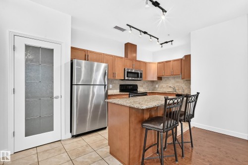 Kitchen featuring stainless steel appliances, wood-finish cabinetry, granite-finish countertops, and track lighting - #307 1003 Gault Bv Nw, Edmonton, AB 
