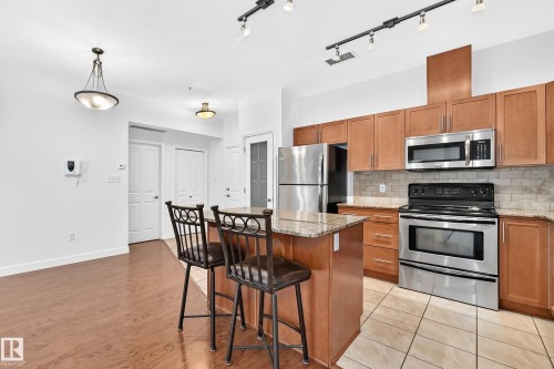Kitchen featuring wood cabinetry, stainless steel appliances, a stone countertop island, and tile flooring - #307 1003 Gault Bv Nw, Edmonton, AB 