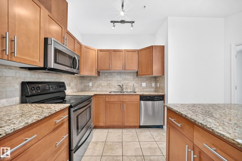 Wood-finish cabinetry paired with granite countertops, stainless steel appliances, and a tiled backsplash - #307 1003 Gault Bv Nw, Edmonton, AB 
