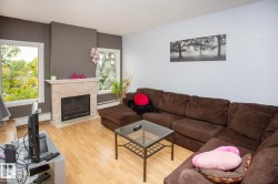 Living area featuring wood-finish flooring, a fireplace with a light-toned surround, and multiple windows - 