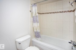 White bathtub with chrome fixtures, tiled shower surround with accent band, and a white toilet - 