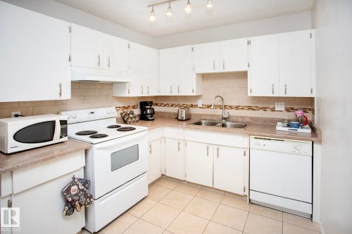 White cabinetry with brushed nickel hardware, stone-finish countertops, and a tiled backsplash - #407 9810 178 St Nw, Edmonton, AB 