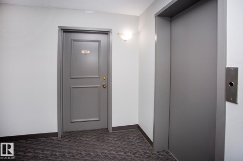 Elevator access, wall-mounted light fixture, paneled door, dark gray carpeting, and light gray wall finishes - #407 9810 178 St Nw, Edmonton, AB 