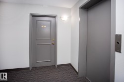 Elevator access, wall-mounted light fixture, paneled door, dark gray carpeting, and light gray wall finishes - 
