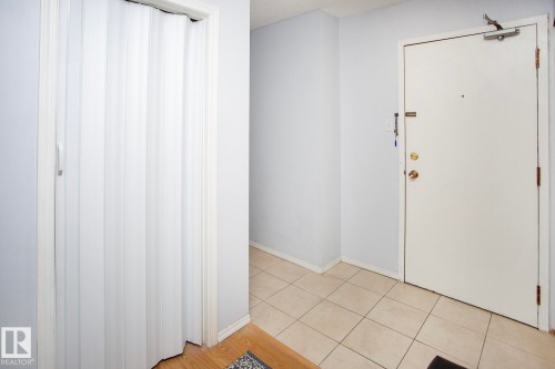 Entryway featuring a white accordion door, white interior door, and square tile flooring - #407 9810 178 St Nw, Edmonton, AB 