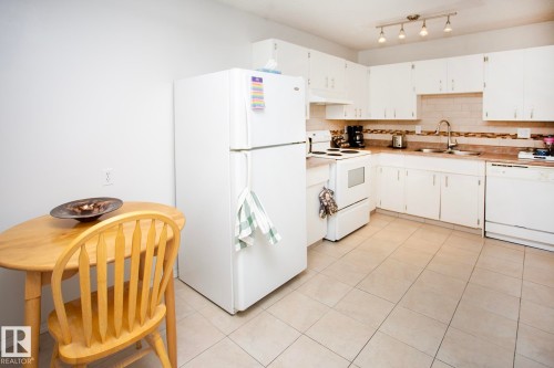 Kitchen featuring white cabinetry, subway tile backsplash, track lighting, stainless steel sink, and tile flooring - #407 9810 178 St Nw, Edmonton, AB 