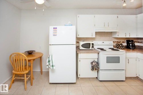 Kitchen featuring white cabinetry, light-colored countertops, tile backsplash, and tile flooring - #407 9810 178 St Nw, Edmonton, AB 