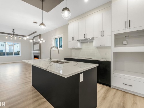 Modern kitchen featuring a large island with an integrated sink, white cabinetry, contrasting dark lower cabinets, and wood-finish flooring - 36 Dalquist Bay, Leduc, AB 