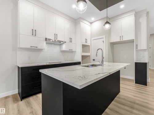 Kitchen featuring a large island with sink, extensive cabinetry, white subway tile backsplash, and wood-finish flooring - 36 Dalquist Bay, Leduc, AB 