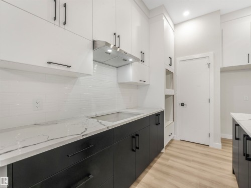 Contemporary kitchen featuring two-tone cabinetry, a white subway tile backsplash, light-toned wood-finish flooring, and white countertops with dark veining - 36 Dalquist Bay, Leduc, AB 