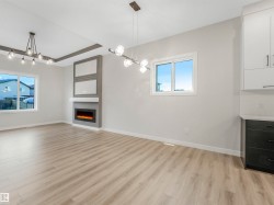 Laminate wood-finish flooring, recessed ceiling detail, built-in fireplace with mantel, white framed windows, and modern pendant lighting - 