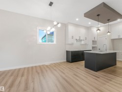 Open concept kitchen and dining area with wood-finish flooring, white and dark cabinetry, kitchen island with sink, and recessed and pendant lighting - 