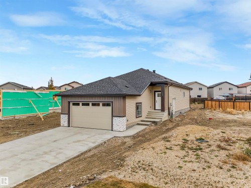 Newly constructed residence featuring a two-car garage, concrete driveway, stone accents, and a covered entry - 36 Dalquist Bay, Leduc, AB 