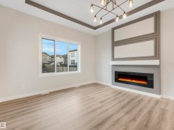 Wood-finish flooring, recessed ceiling with accent trim, contemporary chandelier, electric fireplace, and a large window - 